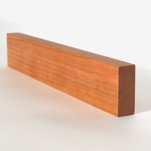 May include: A long, rectangular wooden block with a smooth, light brown finish. The block is made of cherry wood and has a natural grain pattern.