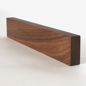 May include: A long, rectangular wooden block made of walnut wood. The wood grain is visible and has a rich brown color.