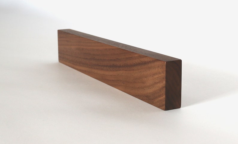 May include: A long, rectangular wooden block made of walnut wood. The wood grain is visible and has a rich brown color.