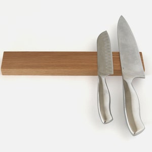 May include: A wooden magnetic knife holder with two silver knives attached. The holder is made of light brown wood and has a smooth surface. The knives are both sharp and have a silver finish.