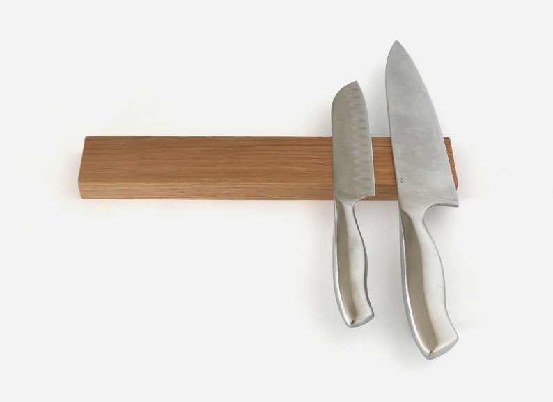 May include: A wooden magnetic knife holder with two silver knives attached. The holder is made of light brown wood and has a smooth surface. The knives are both sharp and have a silver finish.