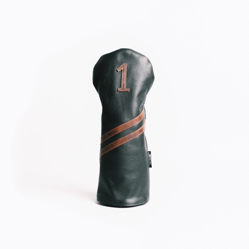 May include: A dark green golf club head cover with brown leather accents. The cover has a brown number 1 and two brown stripes. The cover is made of textured leather and is designed to protect golf clubs.
