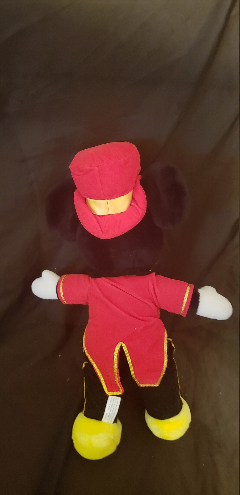May include: A plush toy of Mickey Mouse dressed as a ringmaster. He is wearing a red and gold costume with a black top hat. He has black ears and a white face.