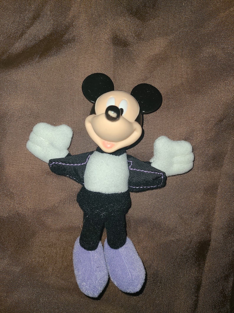 May include: A plush Mickey Mouse toy wearing a black suit with a white shirt and purple shoes.