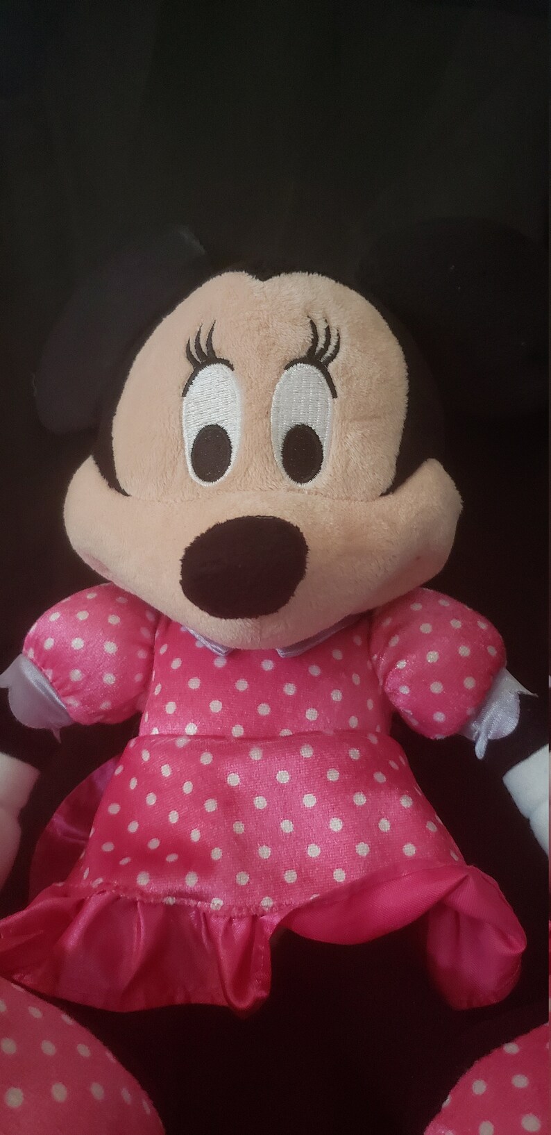 Pu&ograve; includere: Un giocattolo di peluche rosa con pois bianchi, che rappresenta un topo dei cartoni animati con occhi grandi e ciglia nere. Il giocattolo indossa un vestito rosa con un colletto bianco e un orlo arricciato.