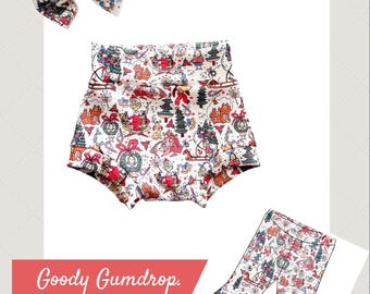 May include: A set of children's clothing featuring a festive Christmas print. The set includes high-waisted shorts, flared pants, and a matching bow. The print features Christmas trees, Santa, and other holiday elements on a white background.