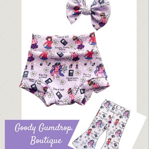 May include: A set of baby clothing items, including a bow, high-waisted shorts, and flared pants, all in a light purple pattern. The pattern features cartoon figures, flowers, and text. The text includes phrases like "Party Animal" and "Boss of Lunch".