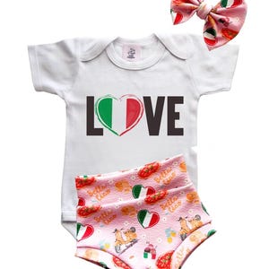 Puede incluir: Body de bebé blanco con la palabra "LOVE" y un diseño de corazón con la bandera italiana. Incluye pantalones cortos rosas a juego con un estampado italiano y un lazo rosa para el pelo.