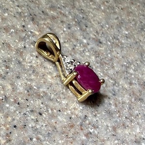 May include: A gold pendant with a ruby gemstone and small diamonds. The ruby is oval-shaped and a deep red color. The pendant has a loop for a chain.