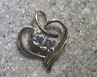 May include: A gold heart-shaped pendant with two blue gemstones and a smaller clear gemstone.