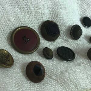 Pode incluir: Conjunto de botões vintage em várias cores e materiais, incluindo preto, marrom, dourado e vermelho. Alguns botões têm designs intrincados, enquanto outros são lisos.