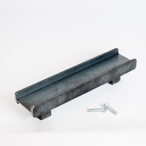 May include: A metal shelf bracket with two mounting points and a slightly curved top edge. The bracket is made of raw steel with a dark gray finish. Two silver screws are included.