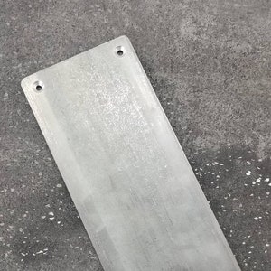 以下が含まれることがあります： 四隅に穴が４つ開いた長方形の金属板。板は銀色で、わずかにざらざらした表面をしています。