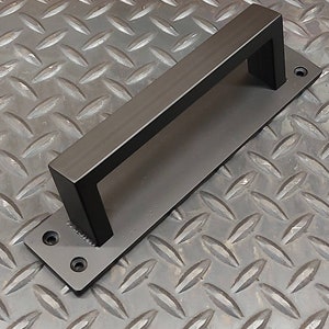 Peut inclure: Poignée de porte en métal noir de forme rectangulaire avec une poignée carrée. La poignée est montée sur une plaque plate avec quatre vis.