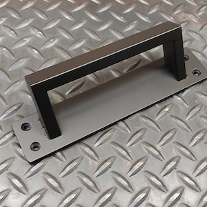 Peut inclure: Une poignée de porte rectangulaire grise mate avec une poignée carrée noire. La poignée a une base rectangulaire avec des trous pré-percés pour le montage. La poignée est de conception simple et moderne.