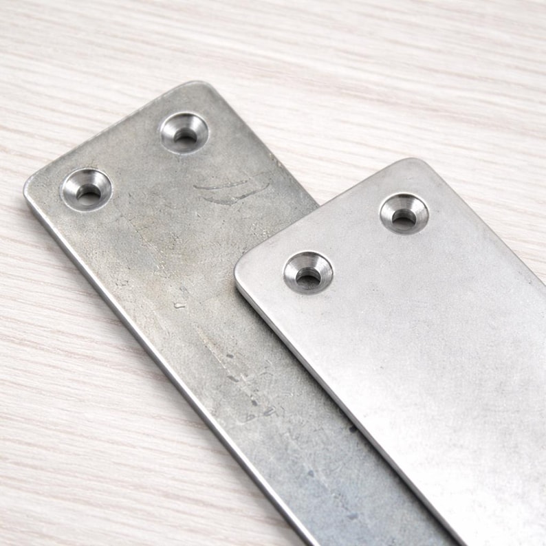May include: Two rectangular metal plates with rounded corners and two pre-drilled holes each. The plates are a brushed silver color and appear to be made of stainless steel. One plate is larger than the other, and they are slightly overlapping.