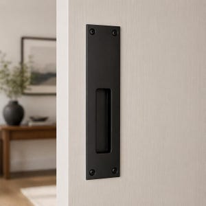 May include: A black rectangular recessed door pull fitted to a light-coloured door. The pull has a rectangular cutout for gripping and is secured with four screws. The door is part of a modern interior.