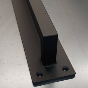 Peut inclure: Poignée de porte en métal noir avec une base rectangulaire et deux trous de fixation. La poignée est conçue pour les portes coulissantes.
