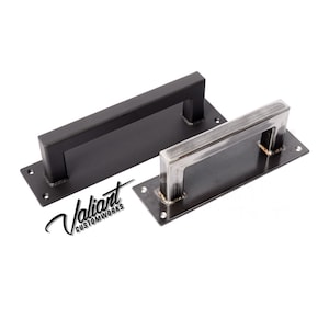 May include: Two metal door pulls. One is black, the other is silver. Both have a rectangular base with a square handle. The text "Valiant Customworks" is in the lower left corner.