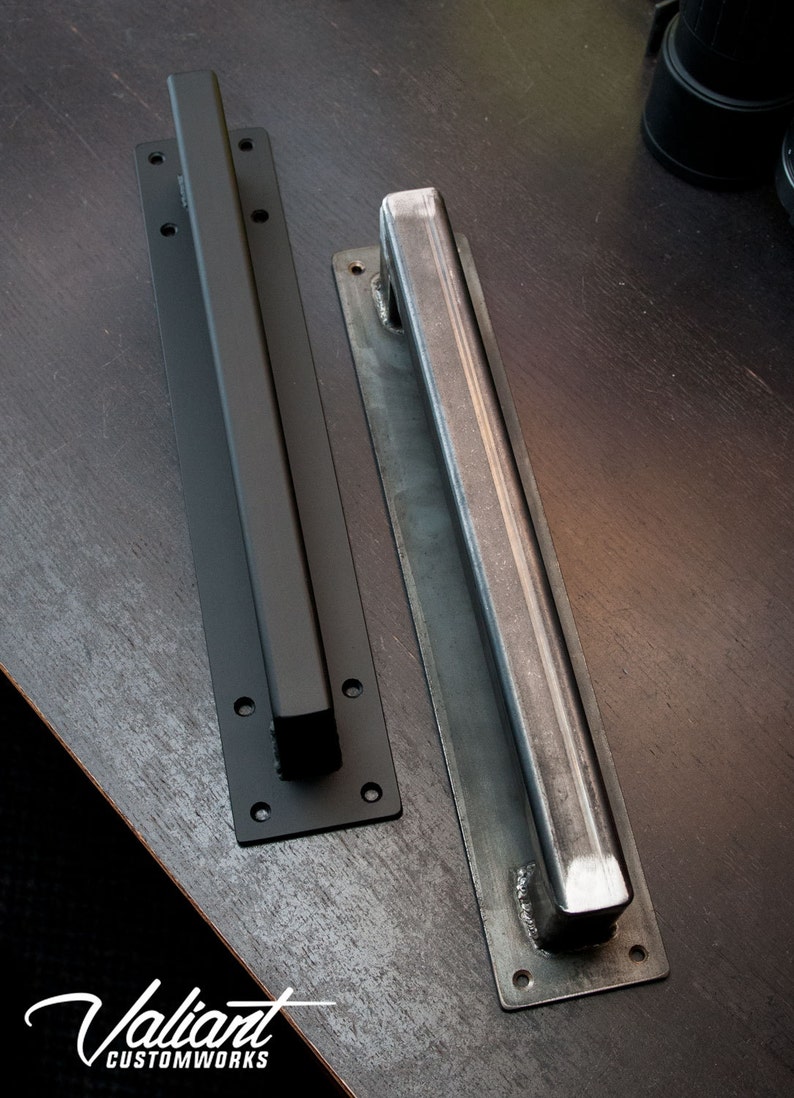 May include: Two metal door pulls. One is black and the other is silver. Both have a rectangular bar handle and a rectangular base with pre-drilled holes for mounting. The logo "Valiant Customworks" is in the bottom left corner.