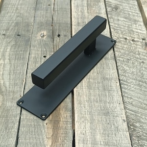 以下が含まれることがあります： 長方形のハンドルと長方形のバックプレートを備えた黒い金属製のドアプル。ハンドルは、4つのネジ穴が付いた長方形のバックプレートに取り付けられています。ドアプルは無垢の金属製で、マット仕上げです。