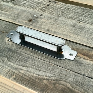 以下が含まれることがあります： テクスチャ加工された長方形のハンドルと装飾的なバックプレートを備えた、銀色の金属製キャビネットプル。ハンドルは2本の垂直ポストで支えられています。ハードウェアはネジで取り付けるように設計されています。