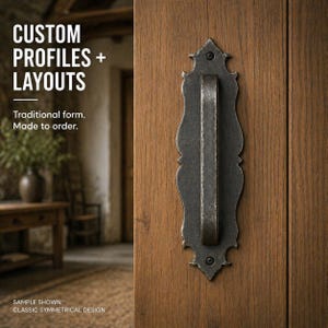 May include: A dark metal door pull with a traditional design is mounted on a wooden door. The door pull has a long, rectangular handle and an ornate backplate. The text "CUSTOM PROFILES + LAYOUTS" is visible.