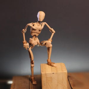 Puede incluir: Una figura de maniquí articulada de color tostado con un acabado liso y mate. La figura presenta una estructura esquelética con rótulas y articulaciones visibles en hombros, codos, muñecas, caderas, rodillas y tobillos en una pose.
