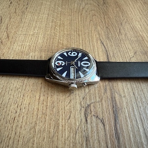 May include: A wristwatch with a black leather band and a dark blue face. The watch has white numerals and hands, with a date display at the 3 o'clock position. The watch case is silver-toned.
