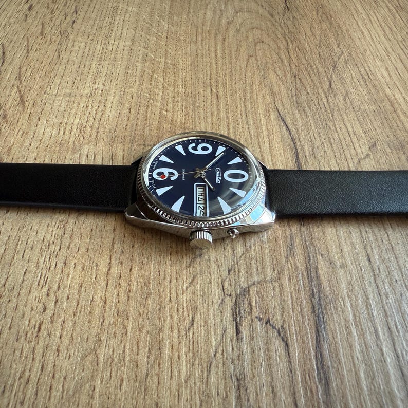 May include: A wristwatch with a black leather band and a dark blue face. The watch has white numerals and hands, with a date display at the 3 o'clock position. The watch case is silver-toned.