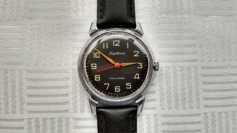 Pu&ograve; includere: Un orologio da polso con quadrante nero, cassa argentata e cinturino in pelle nera. Il quadrante dell'orologio ha numeri bianchi e una lancetta dei secondi rossa. Il marchio dell'orologio &egrave; "Чайка" (Chaika).