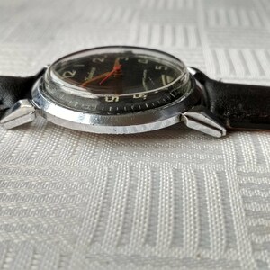 Pu&ograve; includere: Un orologio da polso argentato con quadrante nero e cinturino in pelle nera. L'orologio ha una cassa argentata e una lunetta argentata. Il quadrante dell'orologio ha numeri bianchi e una lancetta dei secondi rossa.
