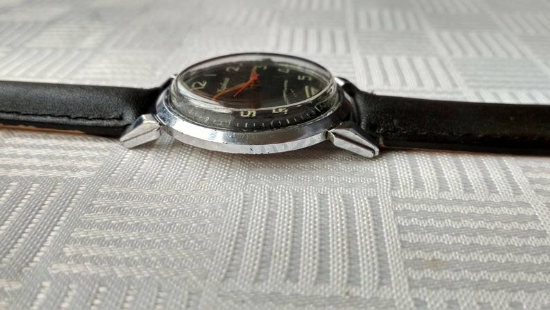 Pu&ograve; includere: Un orologio da polso argentato con quadrante nero e cinturino in pelle nera. L'orologio ha una cassa argentata e una lunetta argentata. Il quadrante dell'orologio ha numeri bianchi e una lancetta dei secondi rossa.