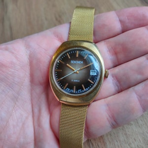 Puede incluir: Reloj de pulsera Sekonda dorado con una correa de malla. La esfera marr&oacute;n tiene agujas e indicadores dorados, y una pantalla de fecha. El reloj est&aacute; etiquetado como "17 Jewels".