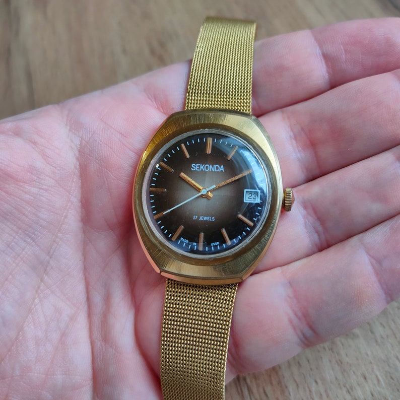 Puede incluir: Reloj de pulsera Sekonda dorado con una correa de malla. La esfera marr&oacute;n tiene agujas e indicadores dorados, y una pantalla de fecha. El reloj est&aacute; etiquetado como "17 Jewels".