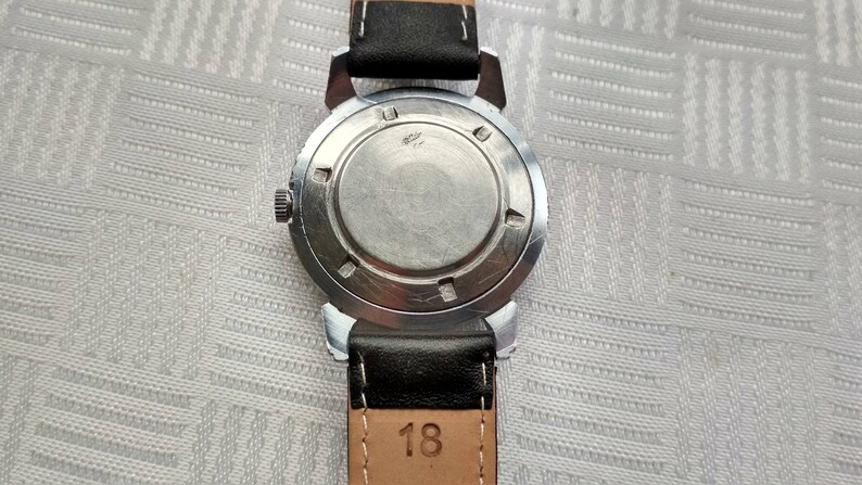 Pu&ograve; includere: Un orologio da polso argentato con un cinturino in pelle nera. Il quadrante dell'orologio &egrave; coperto da una cassa in metallo argentato. Il retro dell'orologio ha il numero "18" stampato.