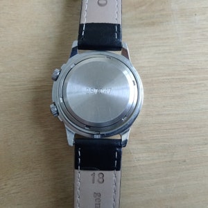 Puede incluir: La parte posterior de un reloj de pulsera plateado con una correa de cuero negro. La esfera del reloj tiene una caja plateada con el n&uacute;mero 297047 impreso en ella. La correa tiene el n&uacute;mero 18 impreso en ella.