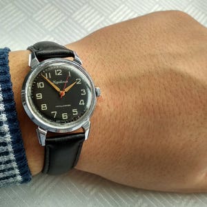 Pu&ograve; includere: Un orologio da polso con quadrante nero, cassa argentata e cinturino in pelle nera. Il quadrante dell'orologio ha numeri bianchi e una lancetta dei secondi rossa. Il marchio dell'orologio &egrave; "Slava" e il testo "Cronografo" &egrave; stampato sul quadrante.