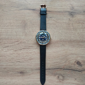 May include: A gold-tone wristwatch with a black leather band and a blue face. The watch has a world time function and a date window.