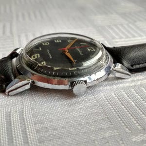 Pu&ograve; includere: Un orologio da polso nero e argento con un cinturino in pelle nera. Il quadrante dell'orologio ha numeri bianchi e una lancetta dei secondi rossa.