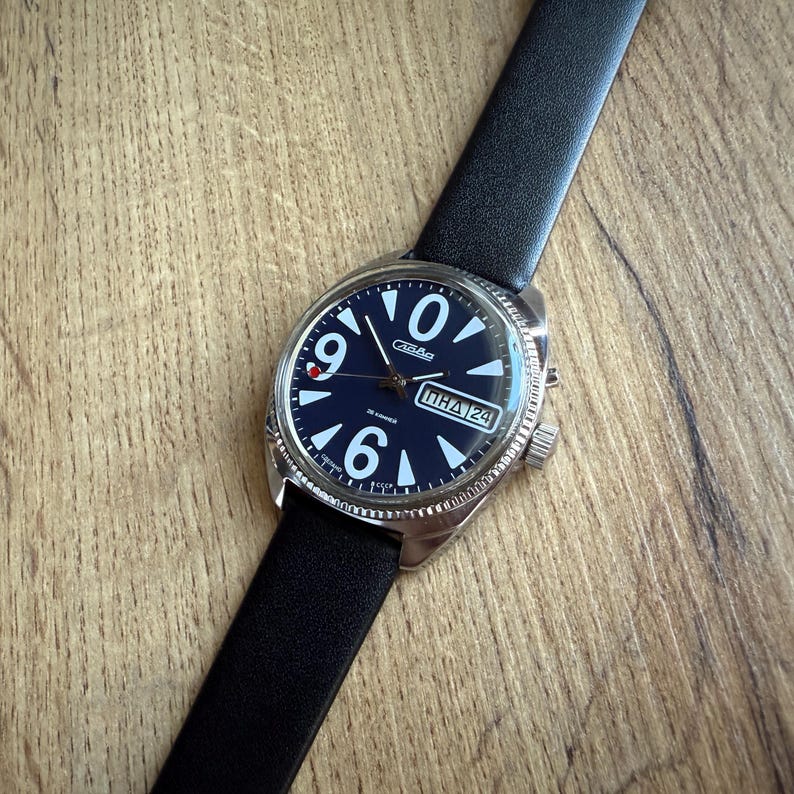 May include: A wristwatch with a black leather band and a navy blue face. The watch has white numerals at the 12, 6, and 9 o'clock positions, with a date display at the 3 o'clock position. The watch case is silver-toned.