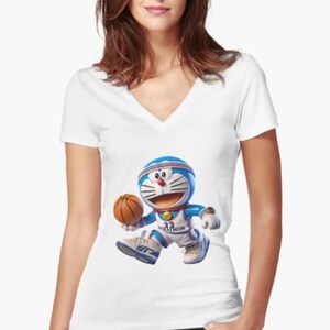 May include: White V-neck t-shirt featuring a cartoon character, Doraemon, in a basketball uniform, dribbling a basketball. The character is blue and white with a red nose and a blue headband. The shirt is worn by a person.