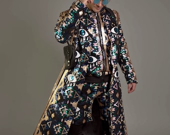 May include: A long black sequined coat with a geometric pattern in gold, blue, and pink. The coat features large eye appliques. The model is wearing black pants and black boots.