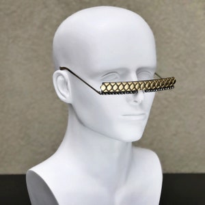May include: A white mannequin head wearing a pair of gold-toned sunglasses with a geometric pattern and black rhinestones.