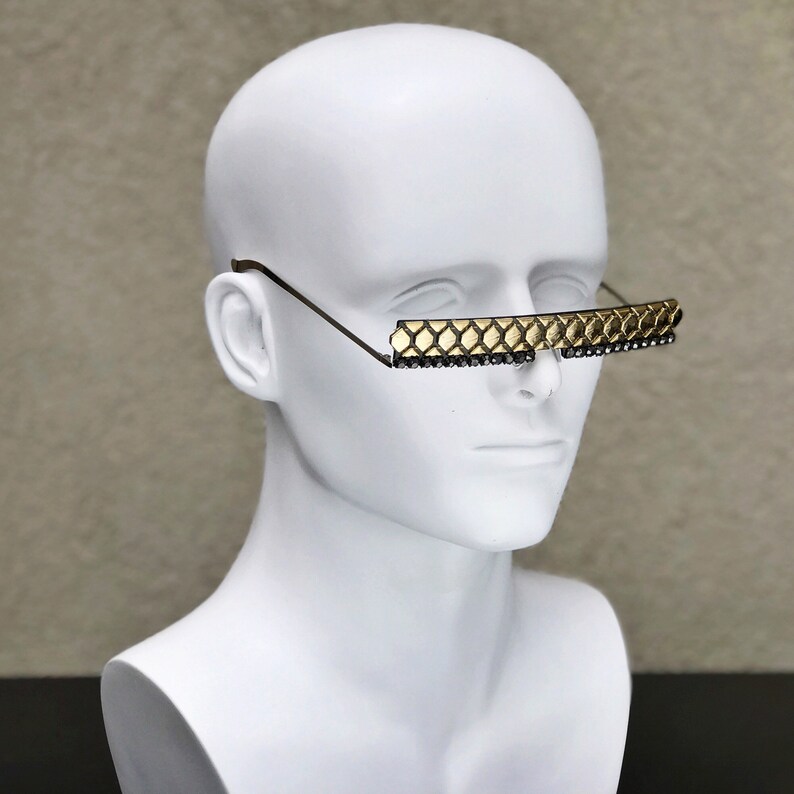 May include: A white mannequin head wearing a pair of gold-toned sunglasses with a geometric pattern and black rhinestones.