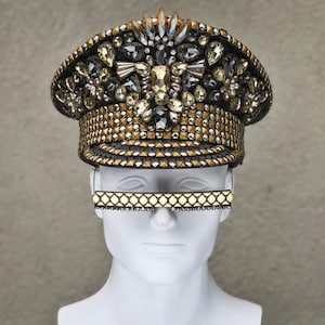 May include: A gold and black embellished hat with a studded brim. The hat is decorated with rhinestones and crystals.