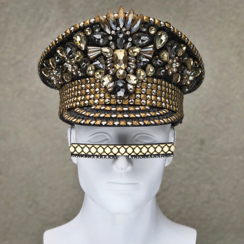 May include: A gold and black embellished hat with a studded brim. The hat is decorated with rhinestones and crystals.