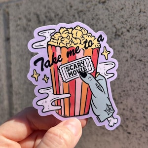 May include: A sticker featuring a cartoon popcorn bucket with the text "Take me to a Scary Movie." A zombie hand holds a movie ticket. The popcorn is yellow, and the bucket is red and orange.