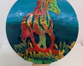 Puede incluir: Una pieza de arte mural redonda y decorativa con la silueta de un caballo. El caballo es una vibrante mezcla de rojo, naranja y verde, con un efecto holográfico. El fondo es azul oscuro con detalles en verde, y la base tiene hierba verde y dorada.