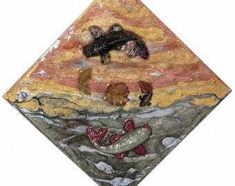 Puede incluir: Una obra de arte en forma de diamante que representa una escena de estanque de carpas koi. La mitad superior tiene un fondo similar a una puesta de sol con tonos dorados, naranjas y rojos. Dos peces koi negros nadan arriba. La mitad inferior es un estanque más oscuro, de color gris, con un pez koi plateado y rojo.